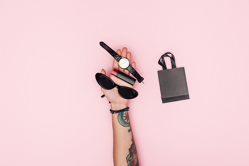 partial view of tattooed girl holding accessories near little shopping bag isolated on pink