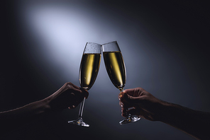 cropped shot of couple clinking glasses of champagne on dark background