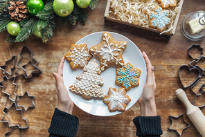 partial view of woman holding plate with homemade cookies on wooden tabletop with decorative christmas wreath and cardboard box