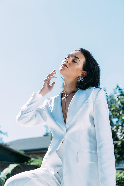 attractive woman in white suit posing with closed eyes outside