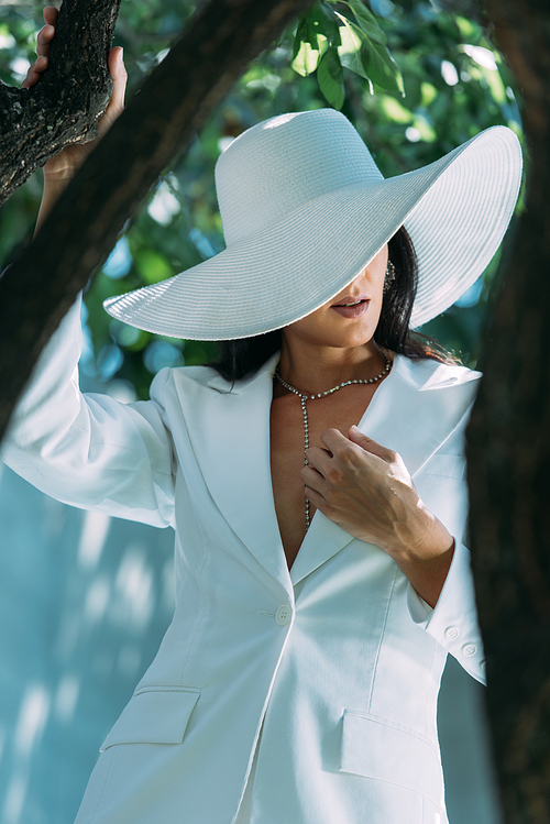selective focus of woman in white suit and hat posing outside