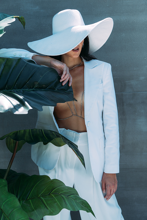 woman in white suit and hat posing and holding leave outside