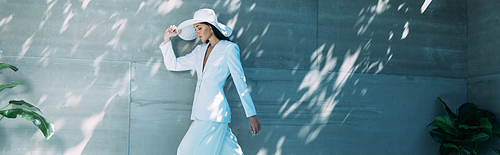 panoramic shot of attractive woman in white suit and hat posing outside