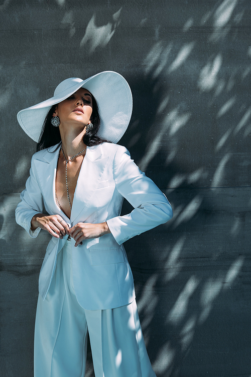 attractive woman in white suit and hat posing with closed eyes outside