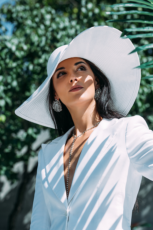 attractive woman in white suit and hat posing and looking away outside