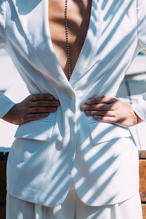 cropped view of woman in white suit posing with hands on hips outside