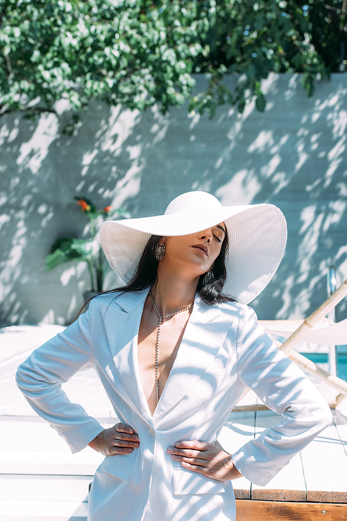 attractive woman in white suit and hat posing with hands on hips outside
