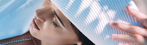 panoramic shot of attractive woman in white hat posing with closed eyes outside