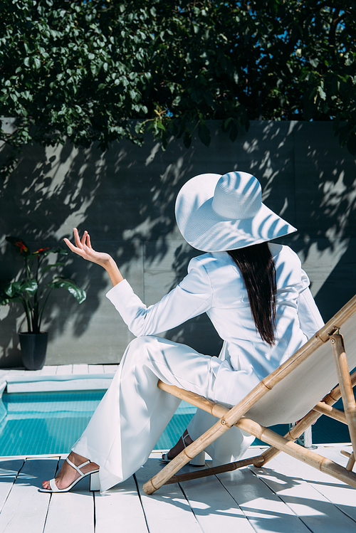 back view of woman in white suit and hat sitting on deck chair outside