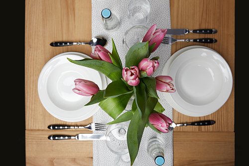 Dinnerware with plates on table with flowers in vase