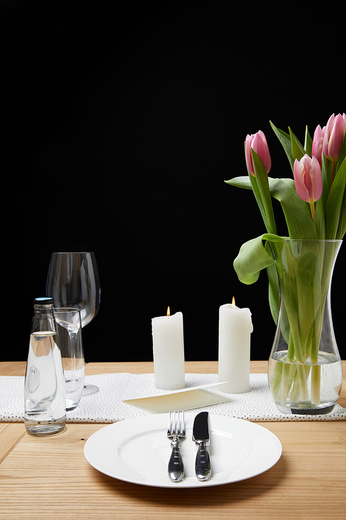 Vase with flower bouquet and candles on table with festive tableware