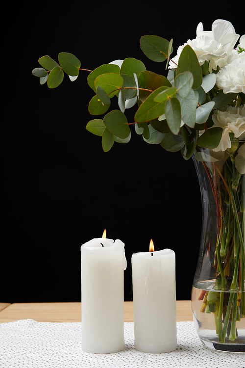 Vase with flower bouquet and candles on table on black background