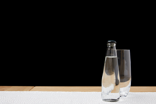 Empty glass and bottle with water on tablecloth on black background