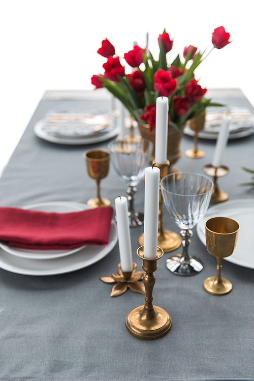 selective focus of candles in vintage candle holders, bouquet of red tulips and arranged empty plates on tabletop