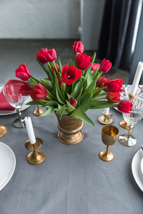 close up view of bouquet of red tulips on tabletop with arranged vintage cutlery and candles
