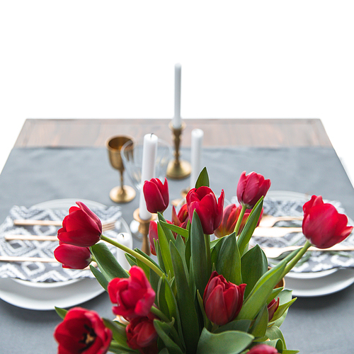 selective focus of bouquet of red tulips and rustic table setting behind