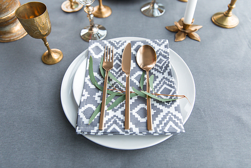 close up view of rustic table setting with vintage tarnished silverware, napkin on plates, green plant and wine glasses