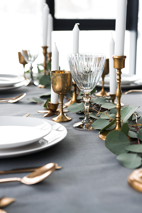 close up view of rustic table arrangement with eucalyptus, vintage cutlery, candles in candle holders and empty plates