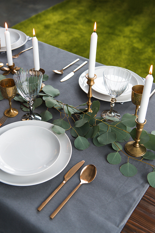close up view of rustic table setting with eucalyptus, vintage tarnished cutlery, candles in candle holders and empty plates