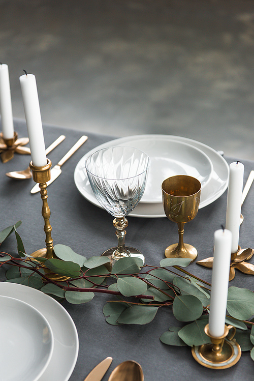 close up view of rustic table setting with wine glasses, eucalyptus, old fashioned cutlery, candles in candle holders and empty plates