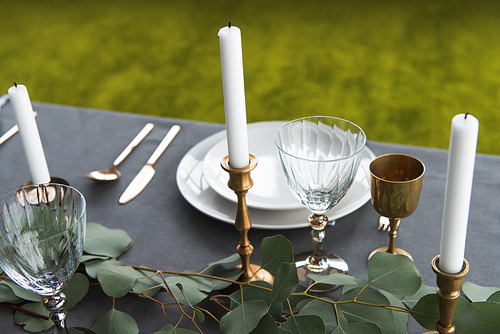 close up view of rustic table setting with wine glasses, eucalyptus, old fashioned cutlery, candles in candle holders and empty plates