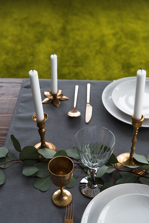 close up view of rustic table arrangement with winecups, eucalyptus, vintage cutlery, candles in candle holders and empty plates