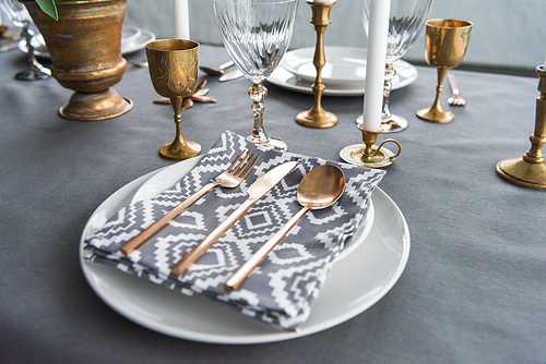 close up view of rustic table setting with old fashioned cutlery and napkin on plates, candles and empty wine glasses on surface