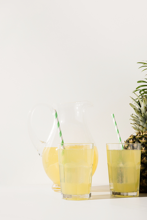 close-up view of glasses and glass jug with fresh juice and ripe pineapple on grey