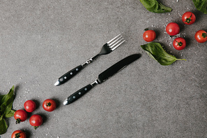 top view of fresh tomatoes, basil and salt with cutlery on grey