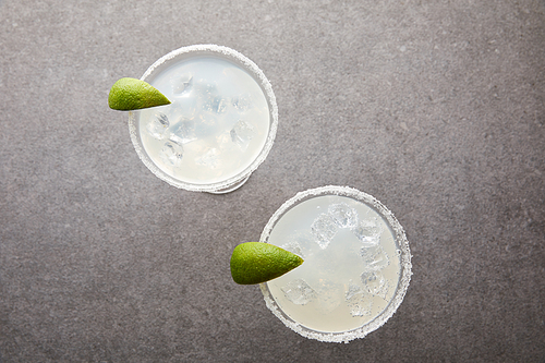 top view of cold alcohol margarita cocktails with pieces of lime on grey tabletop