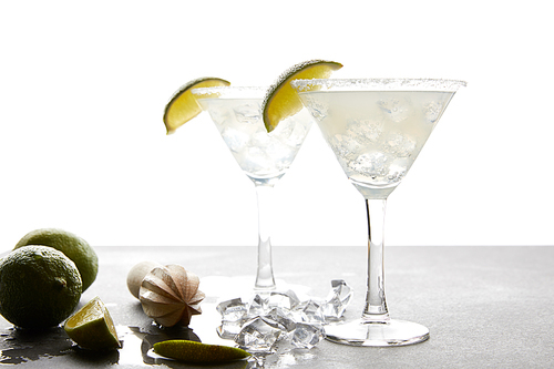 Close up view of margarita cocktails with lime pieces and wooden squeezer on grey surface on white