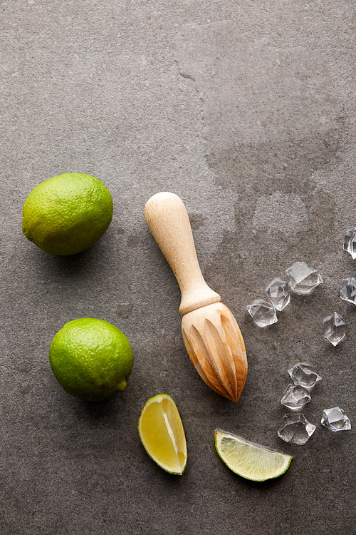 flat lay with wooden squeezer, limes and ice cubes for cocktail on grey surface