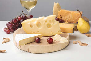 Different types of cheese on wooden boards, wine glass, fruits and almond on gray