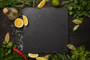 Black slate board with fresh herbs and lemon slices with olive oil