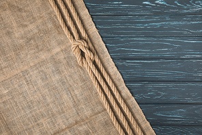 top view of knotted brown nautical rope on sackcloth on wooden background