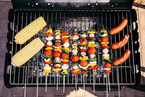 Sausages cooked outdoors on grill with corn and vegetables