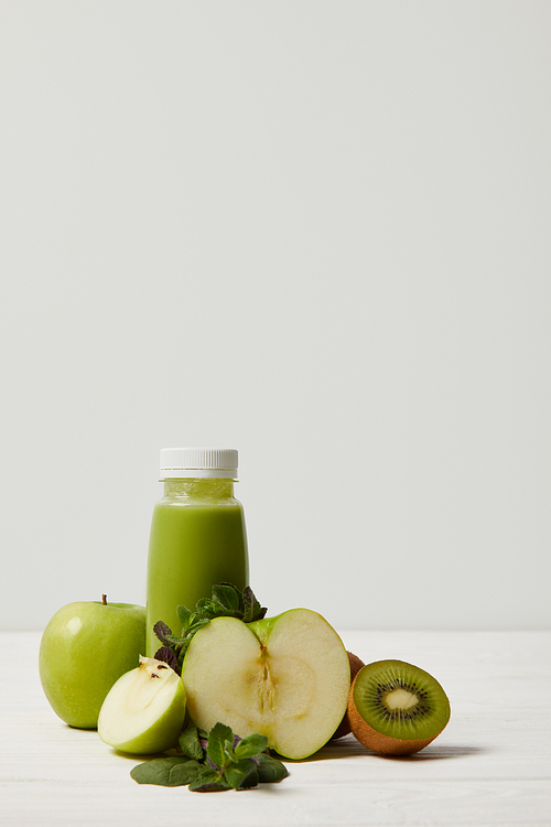 bottle of detox smoothie with green apples, kiwi and mint and on white wooden surface