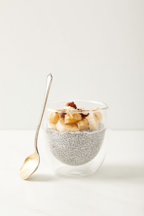 close up view of tasty chia seed pudding with pieces of banana and hazelnuts on white tabletop