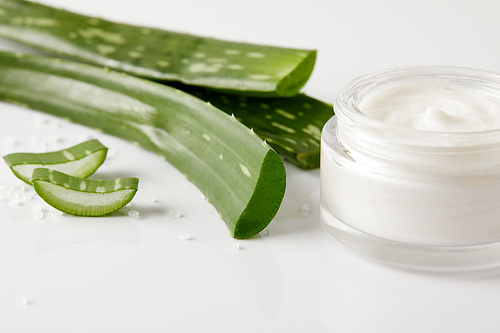 closeup view of organic cream in container, aloe vera leaves and slices on white surface with salt