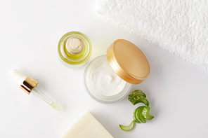 top view of organic cream, cosmetic oil and soap, pipette, towel and aloe vera slices on white surface