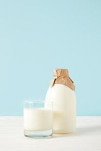 closeup shot of milk glass and milk in bottle wrapped by paper on blue background