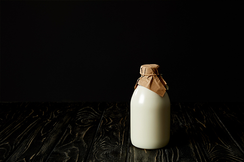 closeup view of fresh milk in bottle wrapped by paper on black background