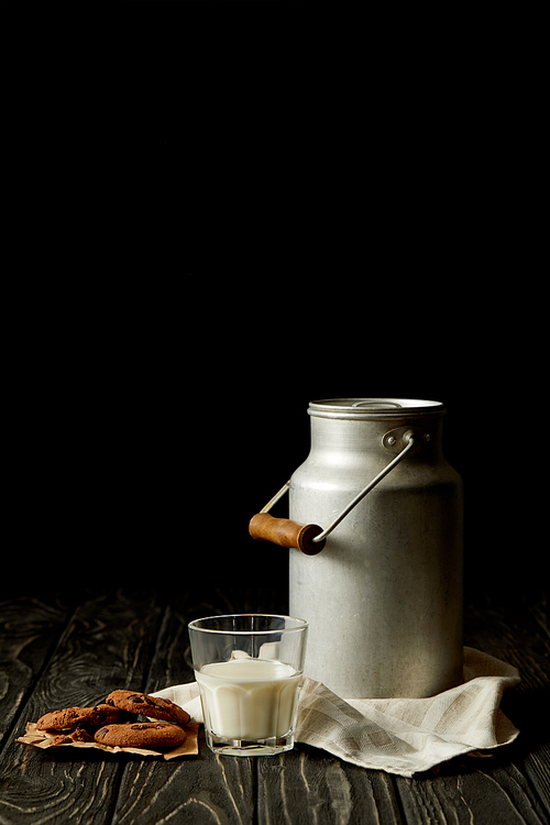closeup view of milk in glass and aluminium can, chocolate cookies and sackcloth on black background