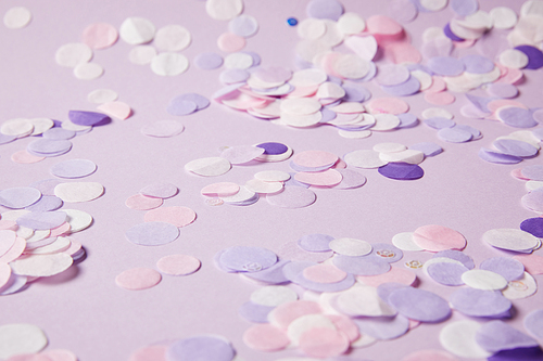 selective focus of confetti pieces on violet surface