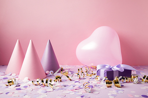 heart shaped balloon, party hats and present on violet tabletop