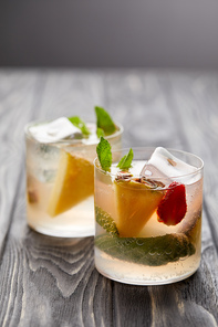 two glasses of lemonade with ice cubes, mint leaves, pineapple pieces and strawberry