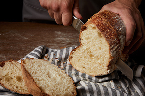 partial view of male baker cutting bread by knife on sackcloth on wooden table