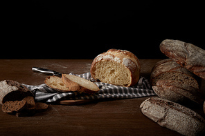 closeup image of various types of bread, sackcloth, knife and cutting board on table