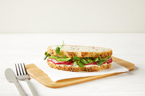 delicious sandwich with radish slices and pea shoots on wooden cutting board