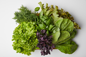 top view of various ripe leaf vegetables in box on white surface